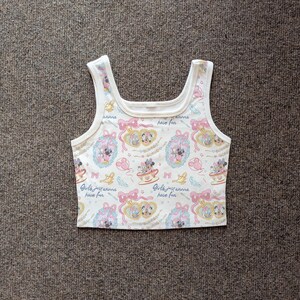 May include: White crop top with a repeating pattern of Minnie Mouse and Daisy Duck in teacups and frames, with pink bows and the text "Girls just wanna have fun". The tank top has a square neckline and white trim.