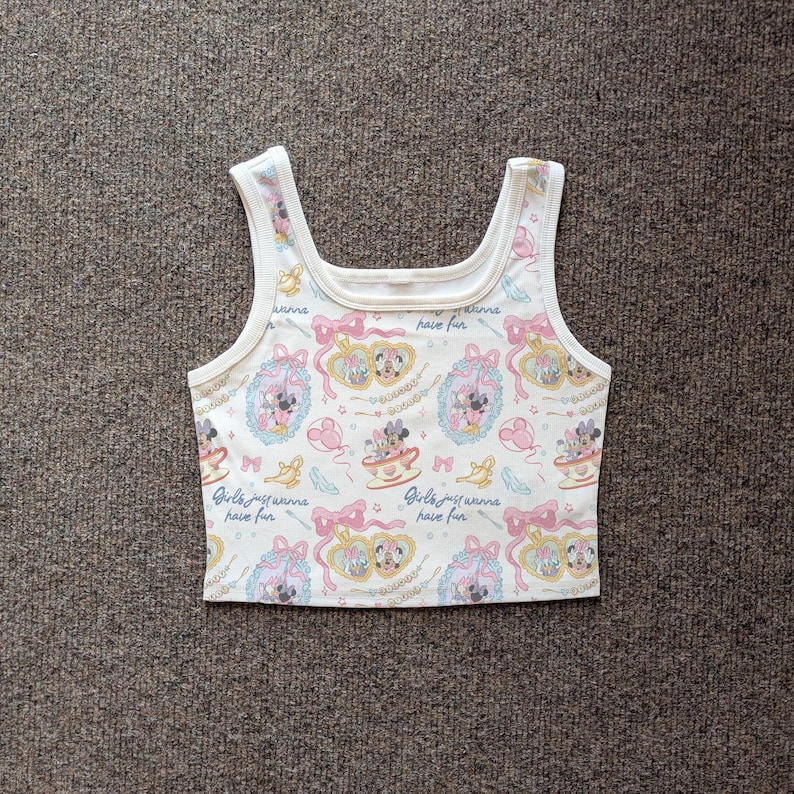 May include: White crop top with a repeating pattern of Minnie Mouse and Daisy Duck in teacups and frames, with pink bows and the text "Girls just wanna have fun". The tank top has a square neckline and white trim.