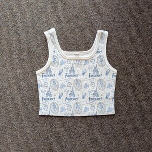 May include: White tank top with a repeating pattern of blue and gray Disney-themed graphics, including castles, Mickey Mouse, and the word "Fantasmic!". The top has a square neckline and wide straps.