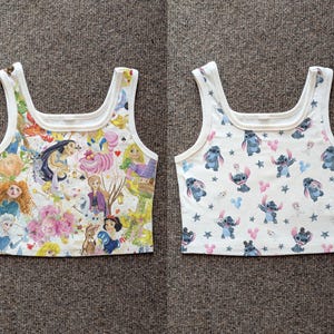 May include: Two white crop tops with a square neckline. One top features a colorful collage of Disney princesses and characters. The other top has a pattern of the character Stitch, with pink and blue accents, and stars.