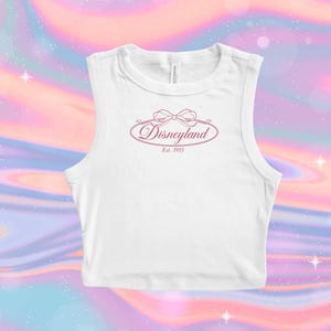 May include: White sleeveless crop top with a pink Disneyland logo. The logo features the word "Disneyland" in a script font, with a bow above and "Est. 1955" below. The background is a colorful, swirling pattern of pink, blue, and purple.