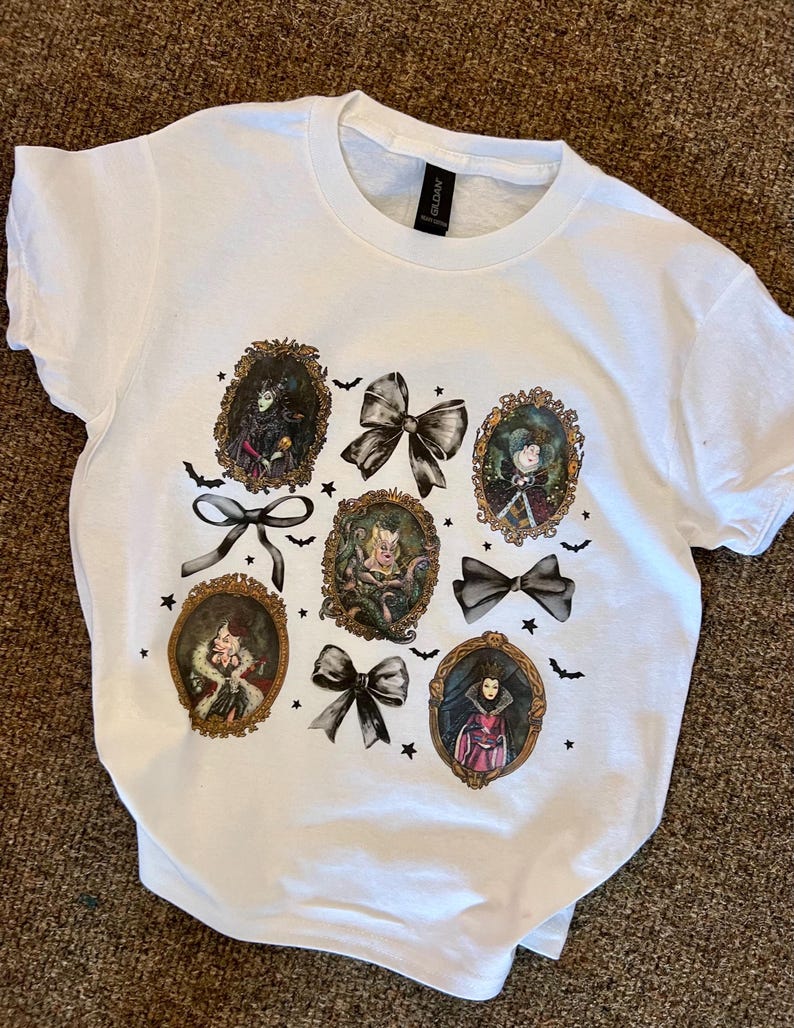 May include: White t-shirt with a print of six Disney villains in gold frames with black bows and bats. The villains are Maleficent, Cruella de Vil, Ursula, Evil Queen, Queen of Hearts, and Hades.