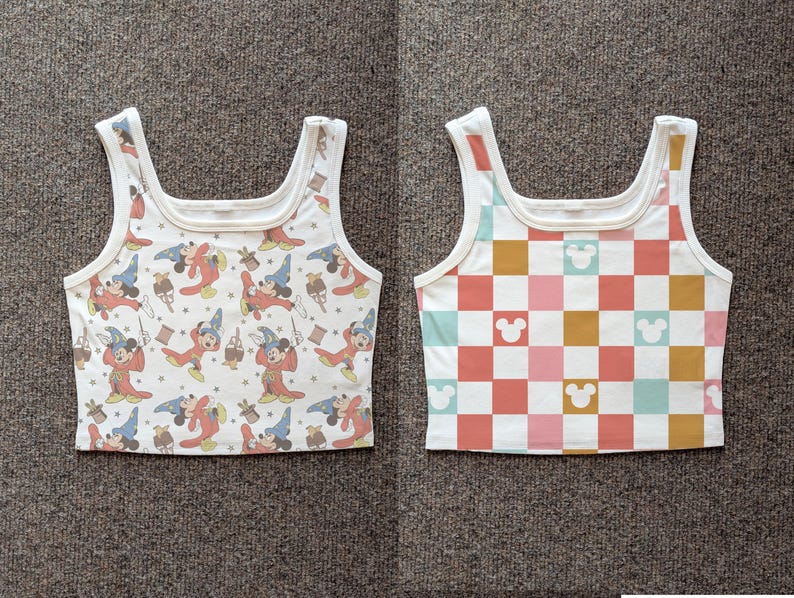 May include: Two white tank tops. One features a pattern of Mickey Mouse as a sorcerer in red and blue robes. The other has a checkerboard pattern in pink, orange, yellow, and teal, with Mickey Mouse silhouettes.