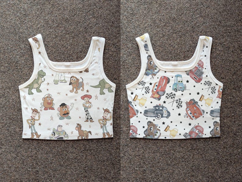 May include: Two white tank tops with a square neckline. One top features Toy Story characters like Woody and Buzz Lightyear. The other top showcases Cars characters, race flags, and stars. Both tops have a repeating pattern.