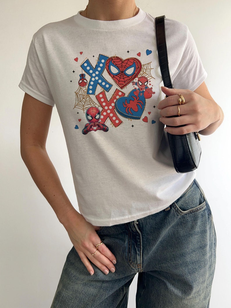Puede incluir: Camiseta blanca con un estampado gr&aacute;fico de Spiderman en un coraz&oacute;n y con las letras X y O. El gr&aacute;fico tambi&eacute;n incluye corazones, telara&ntilde;as y lunares.