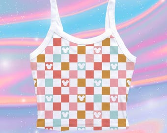 May include: A sleeveless crop top featuring a checkered pattern in shades of pink, light blue, mustard yellow, and white. The design includes small white Mickey Mouse head silhouettes centered within alternating squares across the entire garment.