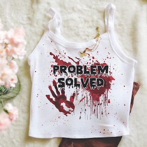 Könnte beinhalten: Weißes Tanktop mit dem Text "PROBLEM SOLVED" in Schwarz, mit roten Blutspritzern und einem Handabdruck-Design. Das Oberteil wird mit einer braunen Hose kombiniert, wodurch ein Halloween- oder Horror-Thema entsteht.