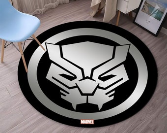 Puede incluir: Alfombra redonda negra y plateada con una cara de pantera negra en el centro. La alfombra tiene un círculo plateado alrededor de la cara de la pantera y la palabra "MARVEL" impresa debajo de la cara.