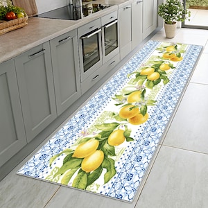 May include: A long kitchen runner rug featuring a lemon branch design. The rug has a white center with a lemon branch and green leaves. The border has a blue and white tile pattern. The rug is rectangular.