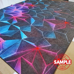 Puede incluir: Una alfombra geom&eacute;trica negra y gris con acentos azules, rosas y rojos. La alfombra tiene un sello "SAMPLE" en la esquina inferior derecha.