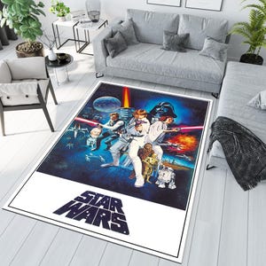 Könnte beinhalten: Ein Star Wars-Teppich mit weißem Hintergrund und dem Star Wars-Logo in Schwarz. Der Teppich zeigt ein blaues und schwarzes Bild der Charaktere aus dem Original-Star Wars-Film, darunter Luke Skywalker, Prinzessin Leia, Han Solo, Chewbacca, Darth Vader und Obi-Wan Kenobi.
