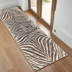 Peut inclure: Un tapis rectangulaire à motif zébré, de couleur marron et crème. Le tapis est posé sur un sol en bois près d'une porte. Le motif zébré présente des rayures marron foncé sur un fond crème. Mesure environ 200 cm de long.