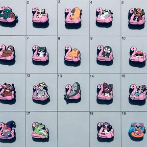 May include: A collection of decorative shoe charms featuring various animal and character designs. Each charm is depicted on a pink flamingo float. The charms include a turtle, cat, bear, penguin, dog, sloth, raccoon, and more.