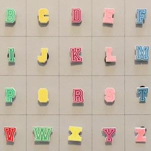 May include: A set of 26 colorful letter tiles, each with a different letter of the alphabet. The tiles are arranged in alphabetical order on a gray background.