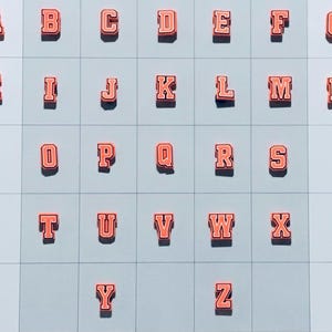May include: A set of 26 orange and white felt letters, A through Z, arranged in a grid pattern. The letters are uppercase and have a varsity style font.