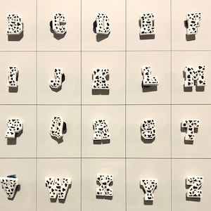 May include: A set of 26 white letters with a black and white cow print design. The letters are arranged in alphabetical order.