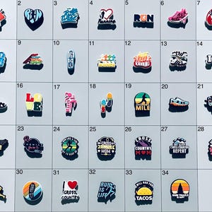 May include: A collection of thirty-three colorful shoe charms featuring various running-themed designs, including sneakers, silhouettes of runners, hearts, and text such as Run, Cross Country, and Just Keep Running, arranged in a grid on a light background.