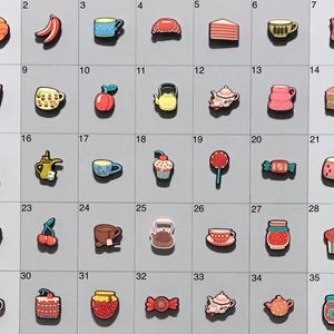 May include: A set of 35 colorful enamel pins featuring various food and drink items, including a croissant, bananas, a mug, a teapot, a cupcake, a lollipop, a candy bar, a pear, a teapot, a cup, a kettle, a cake, a jar of jam, a muffin, and more.