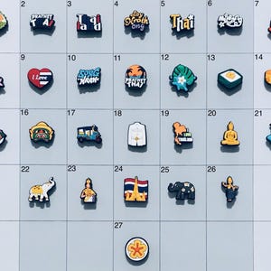 May include: A set of 27 colorful charms featuring Thai culture, including a durian fruit, a temple, a tuk-tuk, a Buddha statue, and the words "Loy Krathong" and "I Love Thailand".