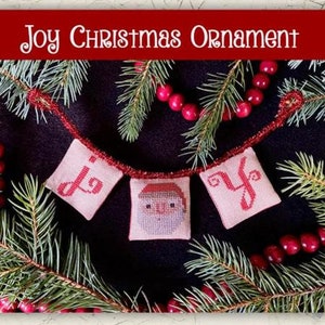May include: Cross stitch pattern for a Christmas ornament featuring a banner with the word "Joy" and a Santa Claus design. The banner is surrounded by green pine branches and red berries.