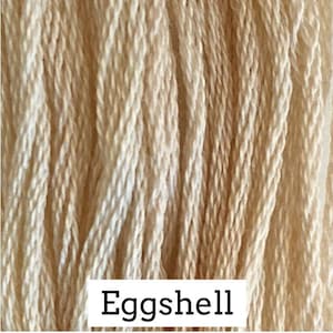 May include: Close-up of a spool of Eggshell colored embroidery floss. The floss is a light cream color.