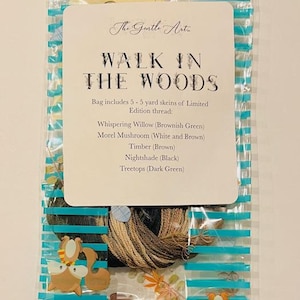 May include: A clear plastic bag with blue stripes contains embroidery thread and a card. The card reads "Walk in the Woods" and lists thread colors: Whispering Willow, Morel Mushroom, Timber, Nightshade, and Treetops. Decorative buttons are visible.