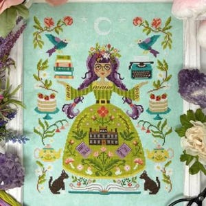 May include: Cross-stitch art featuring a woman with purple hair and glasses, surrounded by books, birds, and cakes. The woman wears a green dress with a house design. The artwork is framed in a white wooden frame.