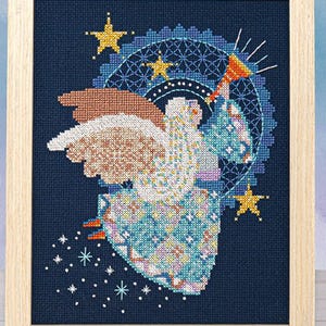 May include: Cross-stitch artwork of an angel playing a trumpet, framed in a light wood. The angel is depicted with detailed wings and a flowing gown, surrounded by stars and a celestial design in shades of blue, brown, and yellow against a dark blue background.