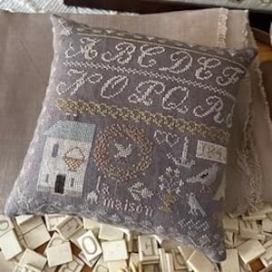 May include: A gray linen pillow with embroidered lettering that reads "Made for You" and "La Maison". The pillow features a small house, a bird in a wreath, a heart, an anchor, and a bird.