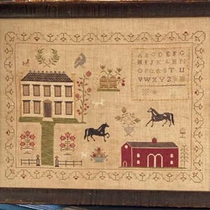 May include: A beige sampler with a cross-stitch design of a house, a barn, horses, and a bird. The sampler also includes a floral design and the alphabet in a rectangular frame.