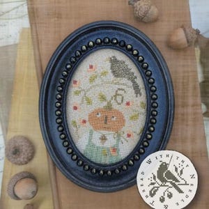 May include: An oval black frame with a beaded edge containing a cross-stitch embroidery of a pumpkin-headed figure and a bird on a branch. A circular white tag with a black bird and branch illustration and the text Thread With Thy Needle is included.