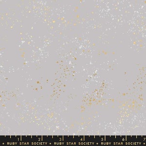 May include: A gray fabric with a scattered pattern of white and gold dots. The fabric is a repeating pattern and is shown with a ruler for scale.