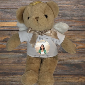 May include: A brown teddy bear wearing a white shirt with the text "A Hug From Heaven When You Need It Most" and a photo of a woman. The bear has angel wings and a gold halo.