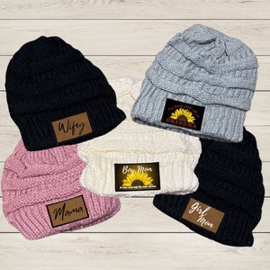 May include: Five knitted beanies with different colored patches. The patches have a sunflower design and text that reads "Wifey", "Mama", "Boy Mom", "Girl Mom", and "Grandma".