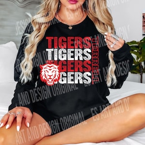 May include: Black long-sleeve shirt featuring the word "TIGERS" in red and white block letters. A red and white tiger head graphic is on the left. The word "HERE" is printed vertically on the right side.