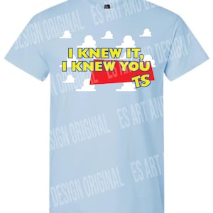 Op de afbeelding: Een lichtblauw T-shirt met korte mouwen en een grafische print van witte wolken tegen een blauwe lucht. De tekst "I KNEW IT, I KNEW YOU TS" is gedrukt in gele letters met een rood rechthoekig accent achter het woord "YOU".