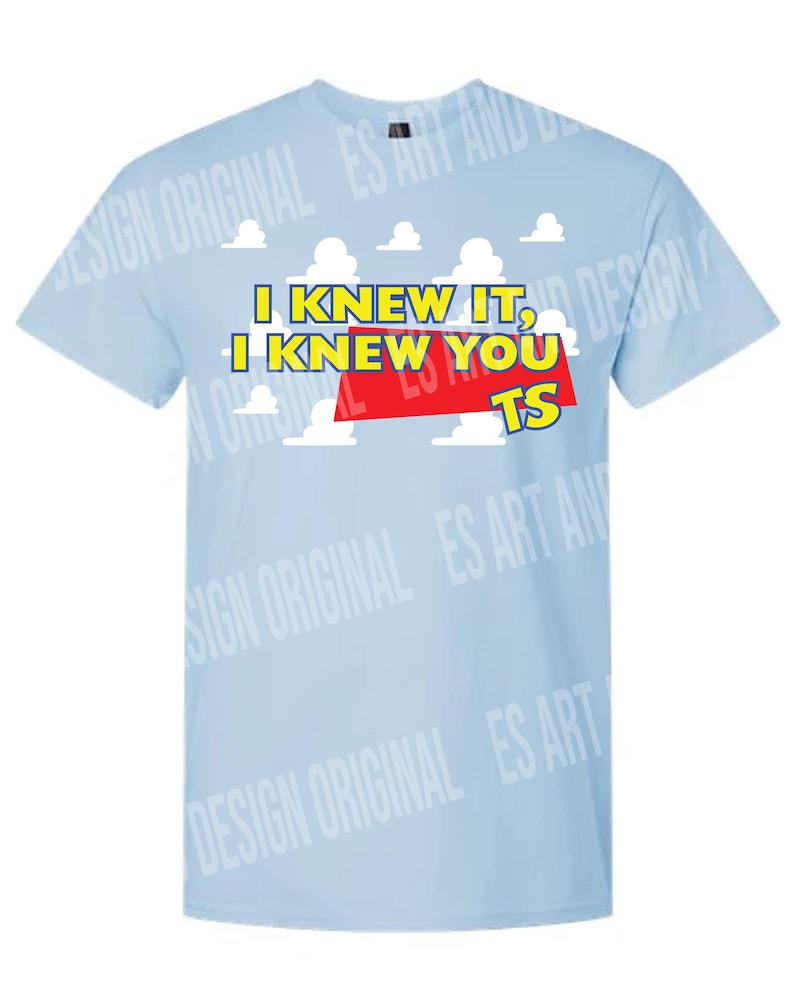 May include: A light blue short-sleeved t-shirt featuring a graphic print of white clouds against a blue sky background. The text "I KNEW IT, I KNEW YOU TS" is printed in yellow letters with a red rectangular accent behind the word "YOU".