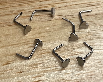 May include: Eight silver nose rings with heart-shaped ends. The rings are arranged in a circle on a wooden surface.