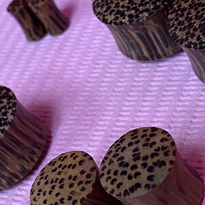 May include: A set of five wooden ear gauges with a black and brown patterned design. The gauges are made of wood and have a smooth finish.