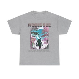 Puede incluir: Una camiseta gris jaspeado con el texto MCBEEVEE sobre un gráfico de una silueta caminando por un bosque con árboles rosas y azules. Debajo del gráfico está el texto: Did I ever show you the trick that I learned from the heathen cannibals to make smoke come out of me ears?