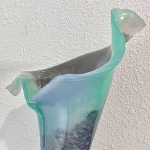 May include: A glass vase with a unique, organic shape. The vase is made of clear glass with a swirling pattern of blue, green, and purple hues.