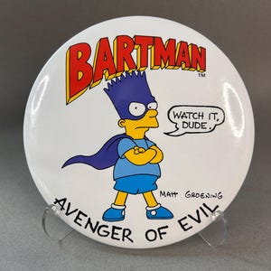 May include: A white button featuring Bart Simpson as Bartman, with a blue mask, cape, and shorts. The text "BARTMAN" in red and yellow is at the top, and "WATCH IT, DUDE." is in a speech bubble. The words "AVENGER OF EVIL" are at the bottom.