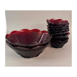 May include: A set of ruby red glass bowls with a scalloped rim. The bowls are stacked in two groups, one with several bowls and another with a few bowls. The bowls have a flower-like shape.