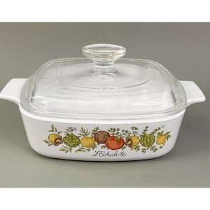 May include: White square casserole dish with a clear glass lid. The dish features a colorful border of illustrated vegetables and the text "L'Echalote". The dish has two white handles.