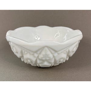 May include: A white, oval-shaped bowl with a detailed, textured exterior. The bowl has a scalloped rim and a decorative pattern around the sides. The bowl is made of a glossy, opaque material.
