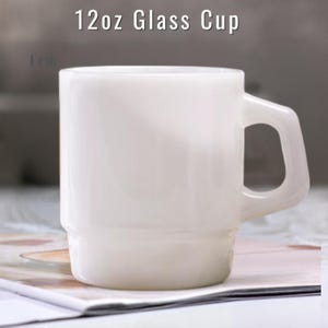 May include: A white 12oz glass cup with a smooth, opaque finish and a sturdy, angular handle. The cup features a cylindrical body with a slightly wider base, designed for stacking. The text 12oz Glass Cup is visible above the object.