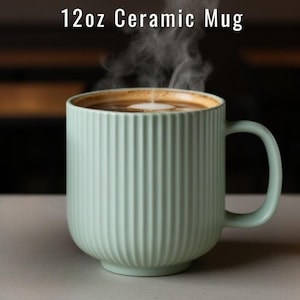 May include: A 12oz ceramic mug in a pale mint green color featuring a vertical ribbed texture on the exterior. The mug is filled with a dark brown liquid topped with a white foam center, and visible steam rises from the top of the beverage.