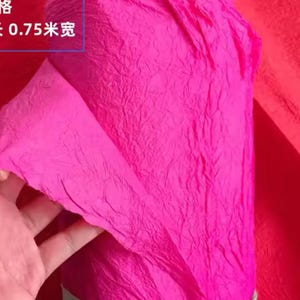 May include: A roll of bright pink crinkle paper, tied with a green ribbon. The paper is textured and has a crinkled appearance. The text on the paper reads "0.75米宽".