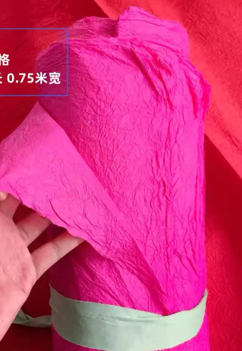 May include: A roll of bright pink crinkle paper, tied with a green ribbon. The paper is textured and has a crinkled appearance. The text on the paper reads "0.75米宽".