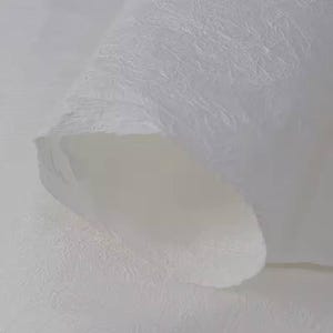 May include: White textured paper with a crinkled, folded edge. The paper has a subtle, embossed pattern.